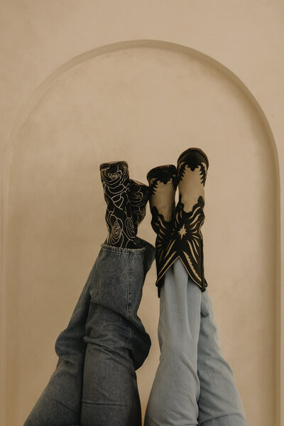 A queer couple (their faces are not pictured), in their cowboy boots and they have their legs up in the air. 