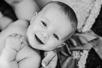 A black and white image capturing a joyful baby smiling brightly at the camera.