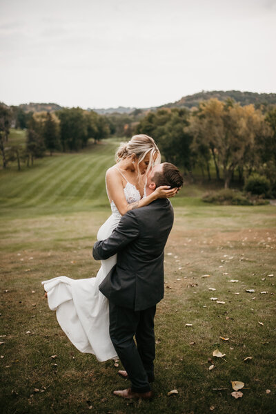 Intimate wedding photo of groom picking up bride and kissing