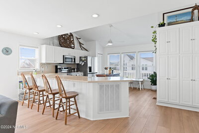 Kitchen counter seating with wooden-backed stools, open view to living room, and balcony overlooking outdoor space.