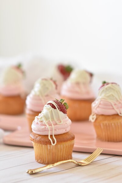 a plate of tiny cupcakes topped with pink frosting and a chocolate covered strawberry with a fork next to one of them for the party planning socialfizz page