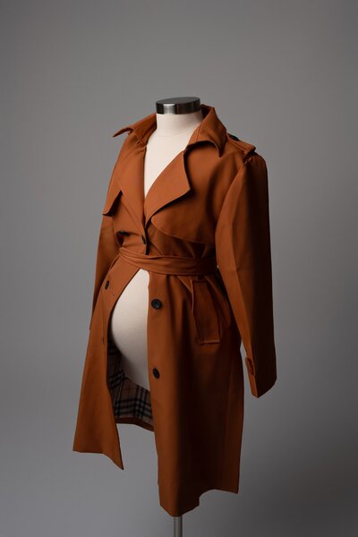 Rust-colored trench coat open over a pregnant belly – editorial maternity accessory available in Austin studio