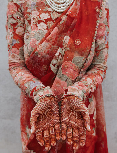 Bride in intricate red saree shows her palms covered in henna on wedding day
