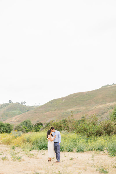 couple stands in outdoor field with wildflowers for Orange County engagement photos