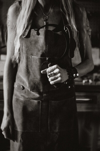 Moody black and white branding portrait of a woman in a leather apron, photographed in a maker’s studio in Breckenridge.