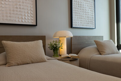 Detail of a secondary bedroom featuring warm wood bedframes, textured bedding, a fluted travertine nightstand with flowers and a book, designed by Sister Studio.
