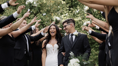 Bride and groom walk through bridal party smiling as flowers are tossed