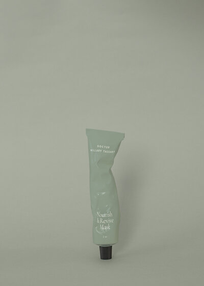 Single sage-green tube labeled ‘Nourish & Revive Mask’ set on a matching background, an example of cohesive beauty brand identity in skincare packaging.