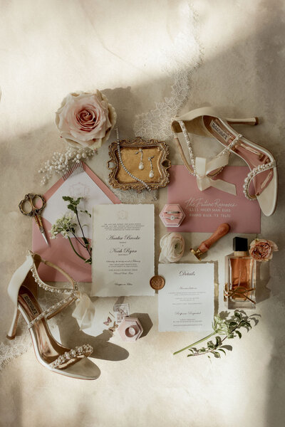Luxury wedding flat lay with bridal heels, blush invitation suite, vintage perfume, and elegant accessories, styled by Eventive Designs in Austin, Texas.