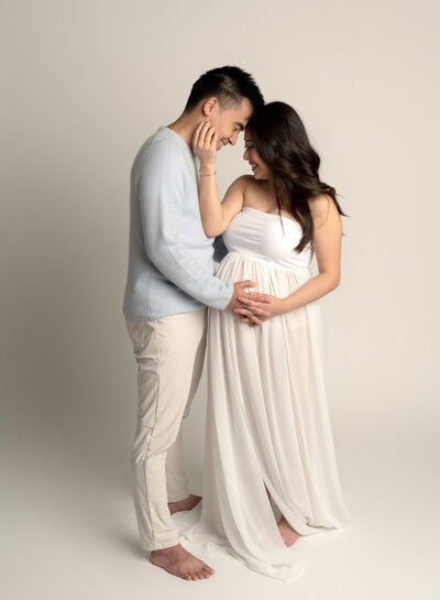 Pregnant couple embracing each other wearing white and light blue