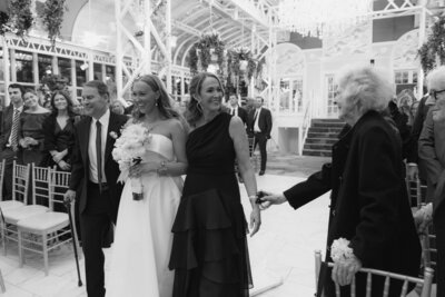 Documentary style photo of bride walking down the aisle with parents and her grandmother reaches out to the mother of the bride at a wedding in Madison, New Jersey.