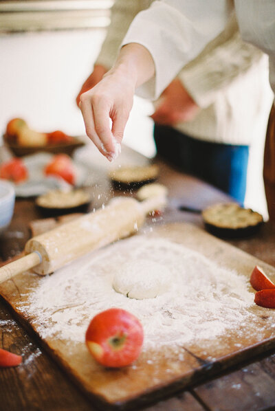 Fluid action shot of woman sprinkling flour over dough to create an apple pie in autumn
