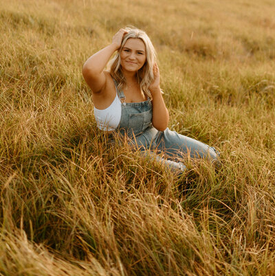 girl sitting in field with overalls on