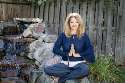 Cyndi sitting in meditation pose outside in a garden