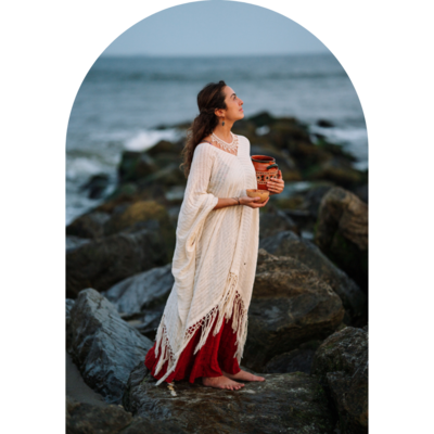 brand photo of a woman standing on rocks at the beach holding an offering of cocoa