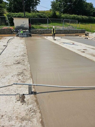 Worker smoothing freshly poured concrete at a construction site.