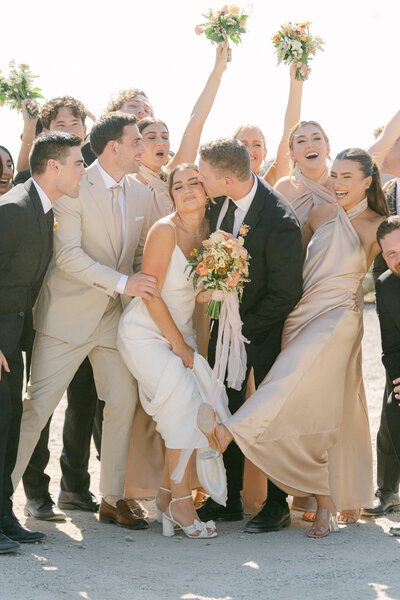 groom kisses bride on the cheek surrounded by cheering wedding party at cielo farms in malibu ca