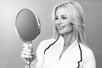 Smiling woman looking in the mirror at her beautifully whitened teeth from WhitenUp Teeth Whitening Spa. 
