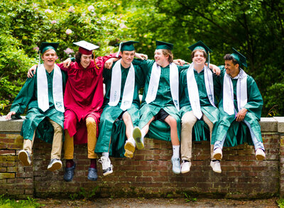 six high school graduation boys sitting on a brick wall laughing