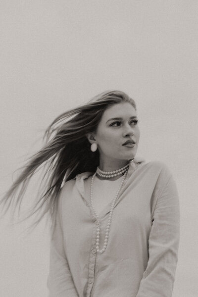 Oklahoma portrait session. Person with long hair and pearls looks away from the camera on a windy day outside