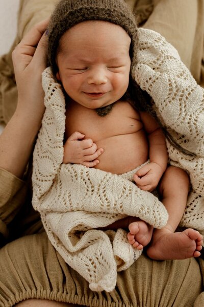 A close-up in soft monochrome of a newborn baby's tiny hand gripping their father's finger, while the mother lovingly looks on. Tender family momen
