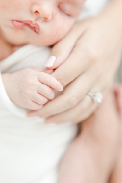 Close up of sleeping newborn holding her mother's fingers