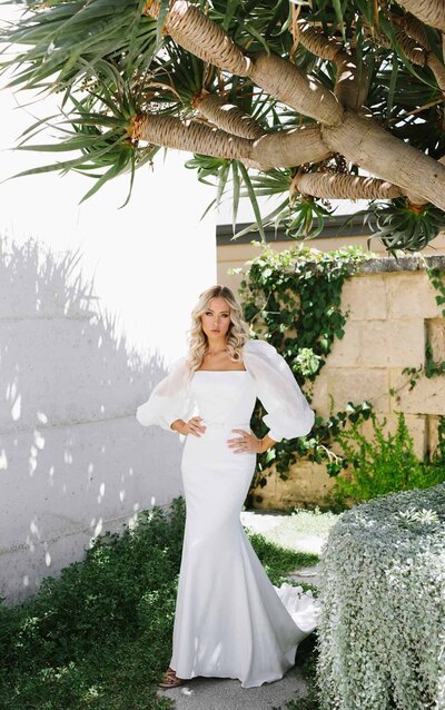 A-LINE WEDDING DRESS WITH SPARKLE A style that incorporates a traditional silhouette with modern detailing, this A-line wedding dress with sparkle from Martina Liana gives you the best of both worlds! Layered lace gives just enough coverage to this bodice while remaining semi-sheer and sexy — creating a nice juxtaposition against the frothy, full skirt. From the empire waist, the lace from the bodice trickles slightly, elongating your silhouette beautifully. A mixture of bugle beading throughout the lace and sparkle tulle within the skirt gives this gown an enviable shimmer, while a horsehair trim gives it a formal, polished look. An open V highlights the back of this bodice, while lace appliques adorn the skirt and train, creating a romantic and dramatic feeling. The back of this A-line wedding dress with sparkle zips up beneath crystal buttons.