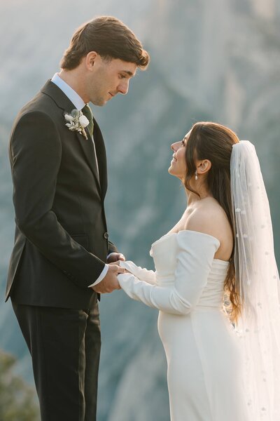 Couple standing at the cliffside edge in Yosemite during their sunrise elopement at glacier point with half dome in the background