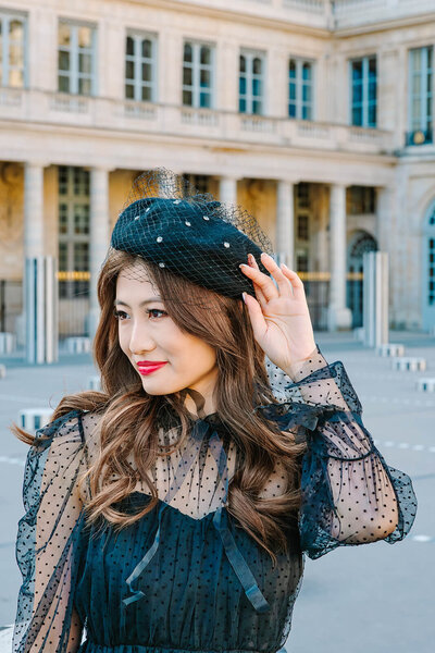 Fashionable solo female traveler adjusting her beret during a Paris photoshoot near the Eiffel Tower, Louvre, and Palais Royal.