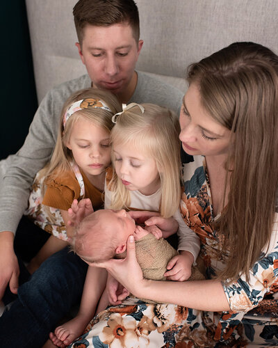 Family of five snuggled on a bed looking at their newborn baby boy.