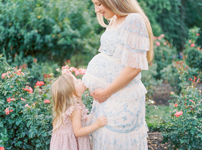 A little girl kisses her mother's belly during their Maryland maternity session in a rose garden