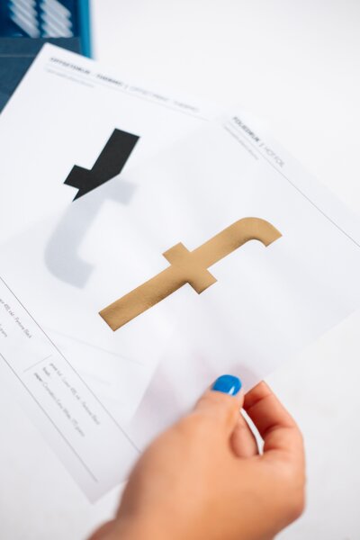 Hand met blauwe nagellak toont transparante folie met gouden letter, branding detail voor Studio Vers huisstijl