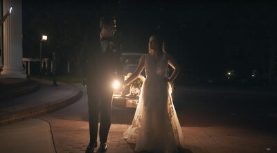 Bride and groom stand and look at eachother in front of a car