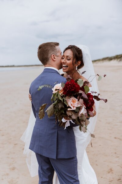Natural wedding photography of two people getting married on the beach holding a large bouquet