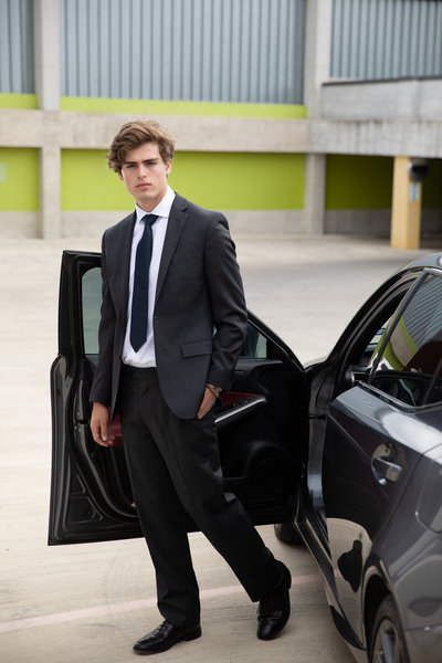 Senior guy wearing a suite standing next to gray car