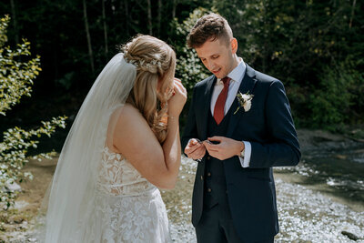 A bride and groom wearing a yellow and green puffy jacket hold each other on top of Rainbow Glacier in Whistler. There is snow all around and blue skies.