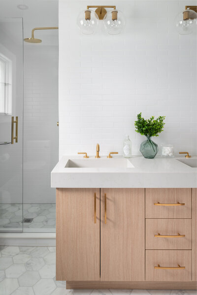 Bathroom thick white slab counter top, wooden cabinets, and all gold light fixtures and hardware.