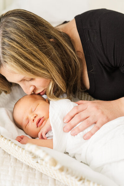 a mother kisses her newborn while on a bed