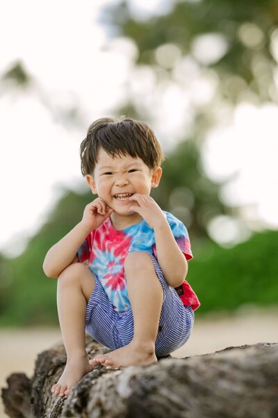 A little boy sits on a rock, smiling.