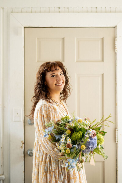 Pittsburgh wedding florist Heavenly Blooms holding a large floral arrangement in front of a cream door