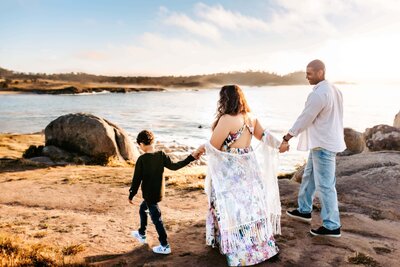 Morgen and her husband hold hands as their young boy walks by the water