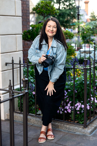 Senior photographer posing with camera leaning up against a rod iron fence in Orlando Florida