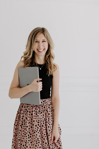 Woman with blonde hair in black tank top and pink polka-dot skirt with laptop