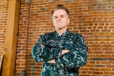 Male Navy veteran standing in front of brick wall with arms folded