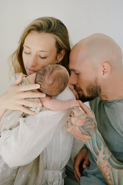 Parents gently kissing their newborn, a beautiful connection in a Sydney family photoshoot