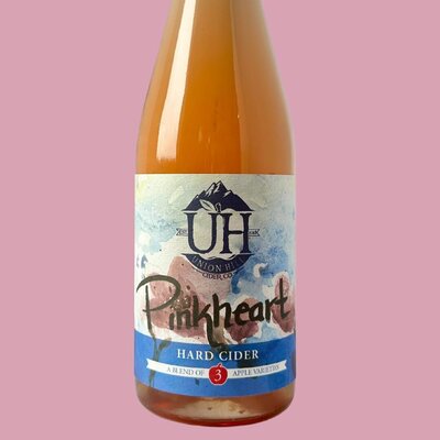 A bottle of Pinkheart hard cider made by Union Hill Cider Co on a pink background