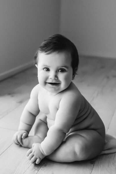 A little baby with lots of chubby baby rolls sitting in the photography studio in taranaki while aimee kelly photographs him