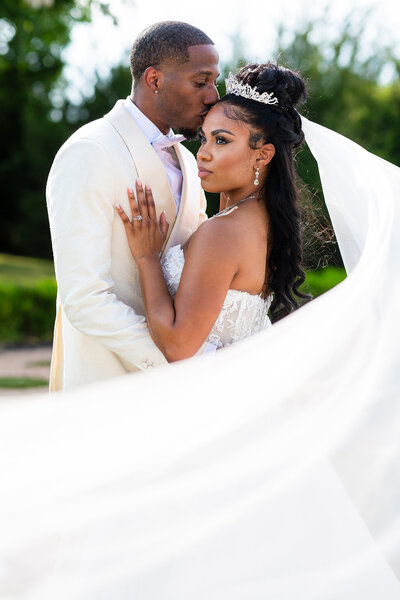 Bride in strapless white wedding gown and long veil smiling up at groom in white tux under a gazebo in a garden during Knotting Hill Place wedding venue in Dallas TX with Stefani Ciotti Photography