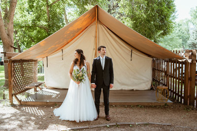 bride and groom stand in front of tent