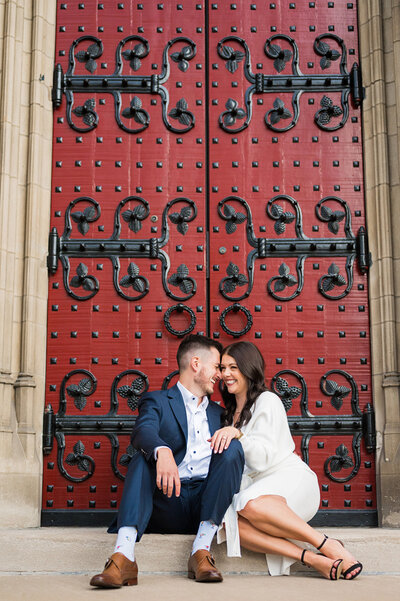 engaged couple snuggling in front of red doors at stephen foster memorial pittsburgh